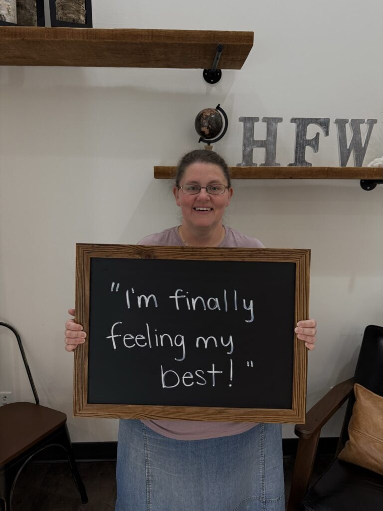A Health From Within patient holding a chalkboard that reads: I'm finally feeling my best!