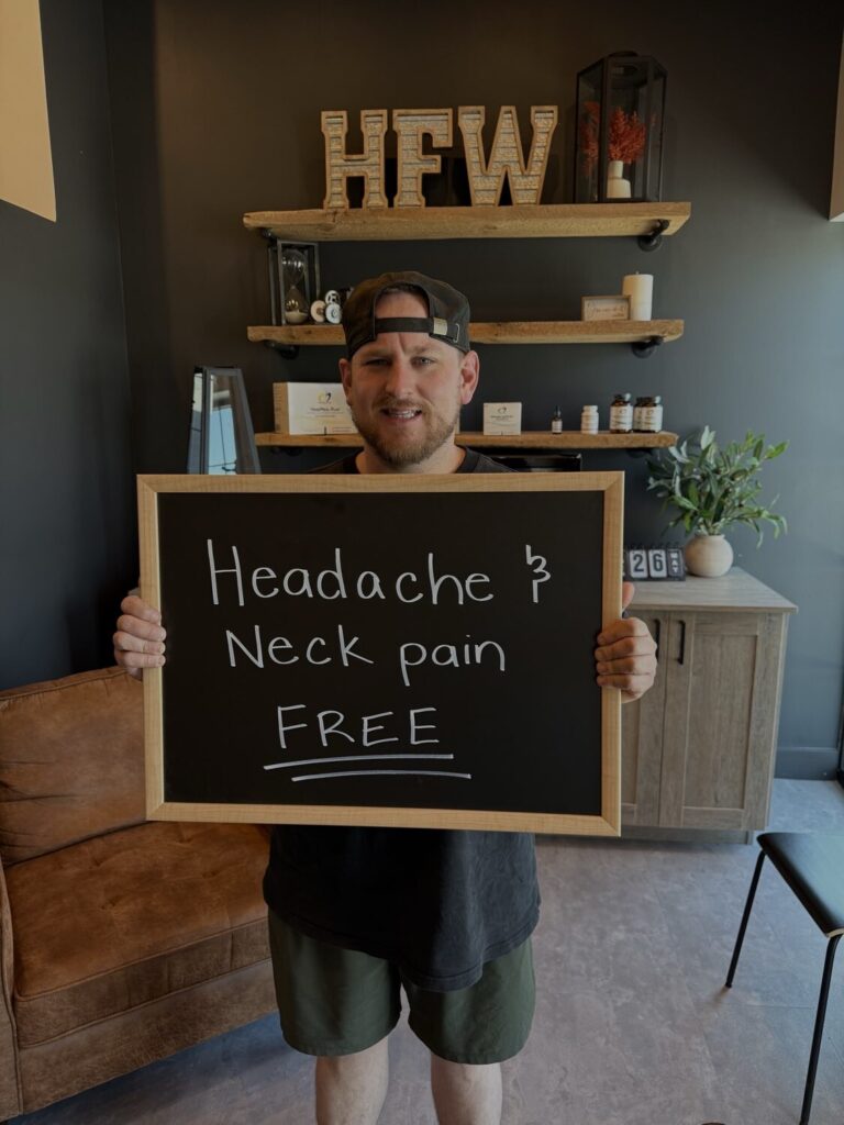 A Health From Within patient holding a chalkboard that reads: Headache and neck pain FREE