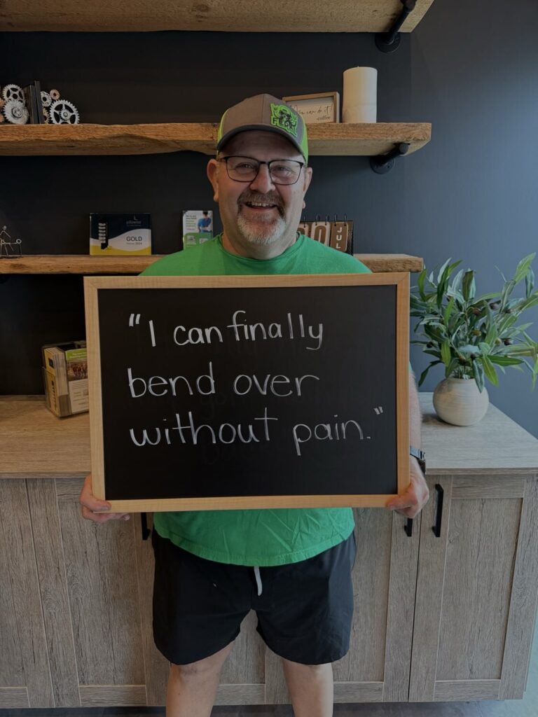A Health From Within patient holding a chalkboard that reads: I can finally bend over without pain.