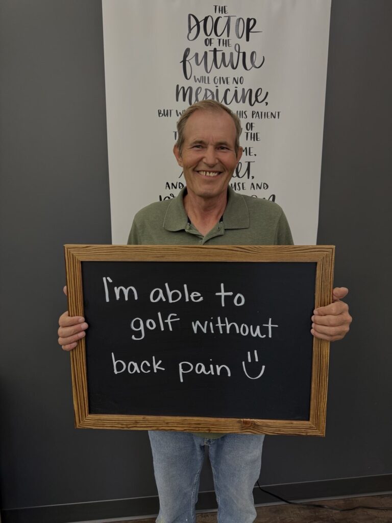 A Health From Within patient holding a chalkboard that reads: I'm able to golf without back pain